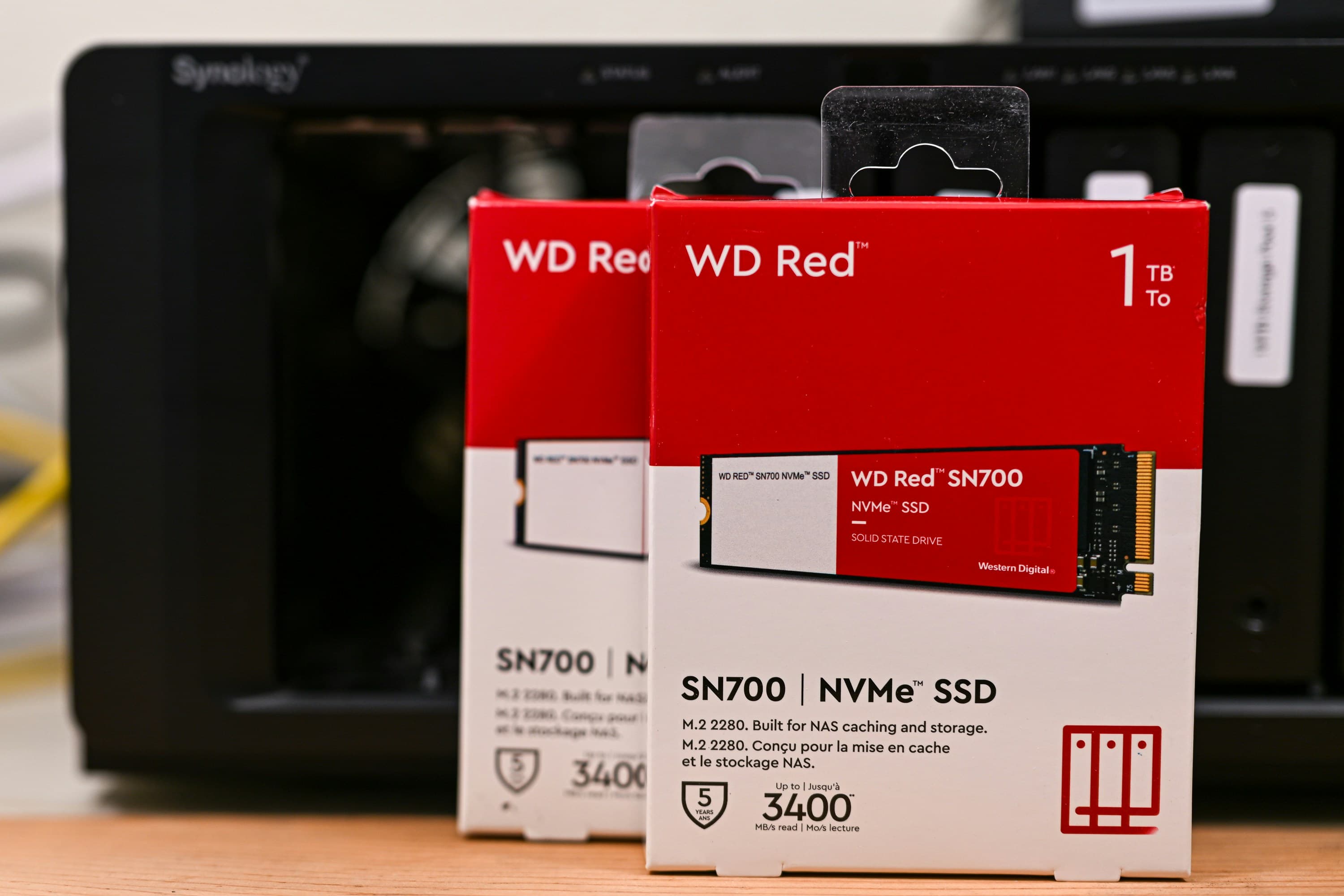Bild von zwei verpackten SSDs (Festplatten). Im Hintergrund ein Netzwerkspeicher